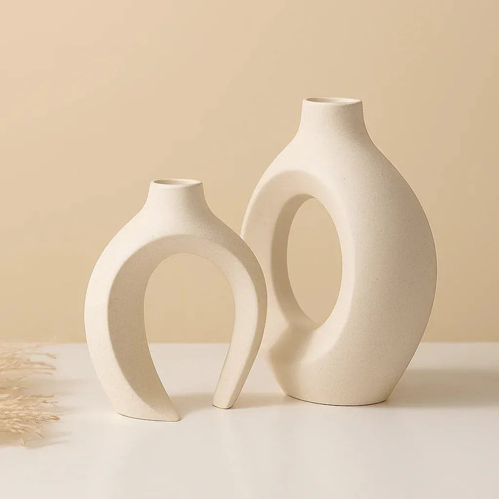 Minimalist round ceramic vase set with abstract sculptural shapes, displayed with colorful fresh flowers on a wooden patio table in a natural outdoor setting