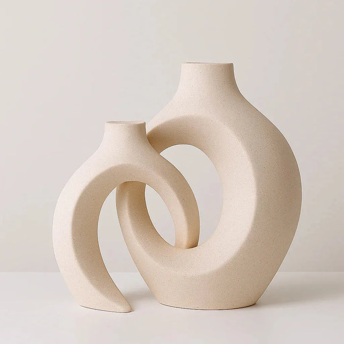 Minimalist round ceramic vase set with abstract sculptural shapes, displayed with colorful fresh flowers on a wooden patio table in a natural outdoor setting