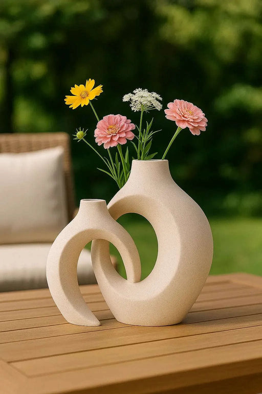 Minimalist round ceramic vase set with abstract sculptural shapes, displayed with colorful fresh flowers on a wooden patio table in a natural outdoor setting